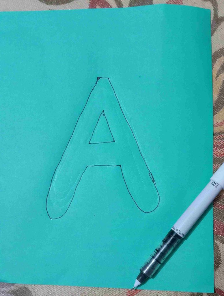 drawing the A letter on the green colored paper with a marker pen